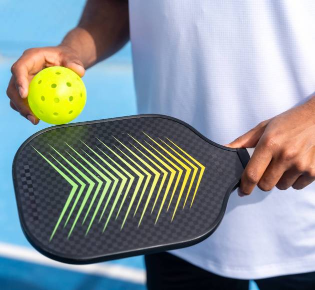 Unrecognizable close-up sportive man with pickleball equipment holding racket and yellow ball in an court